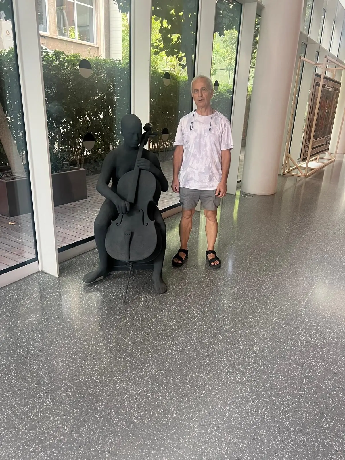 A man beside a statue of a cellist in a bright hall
